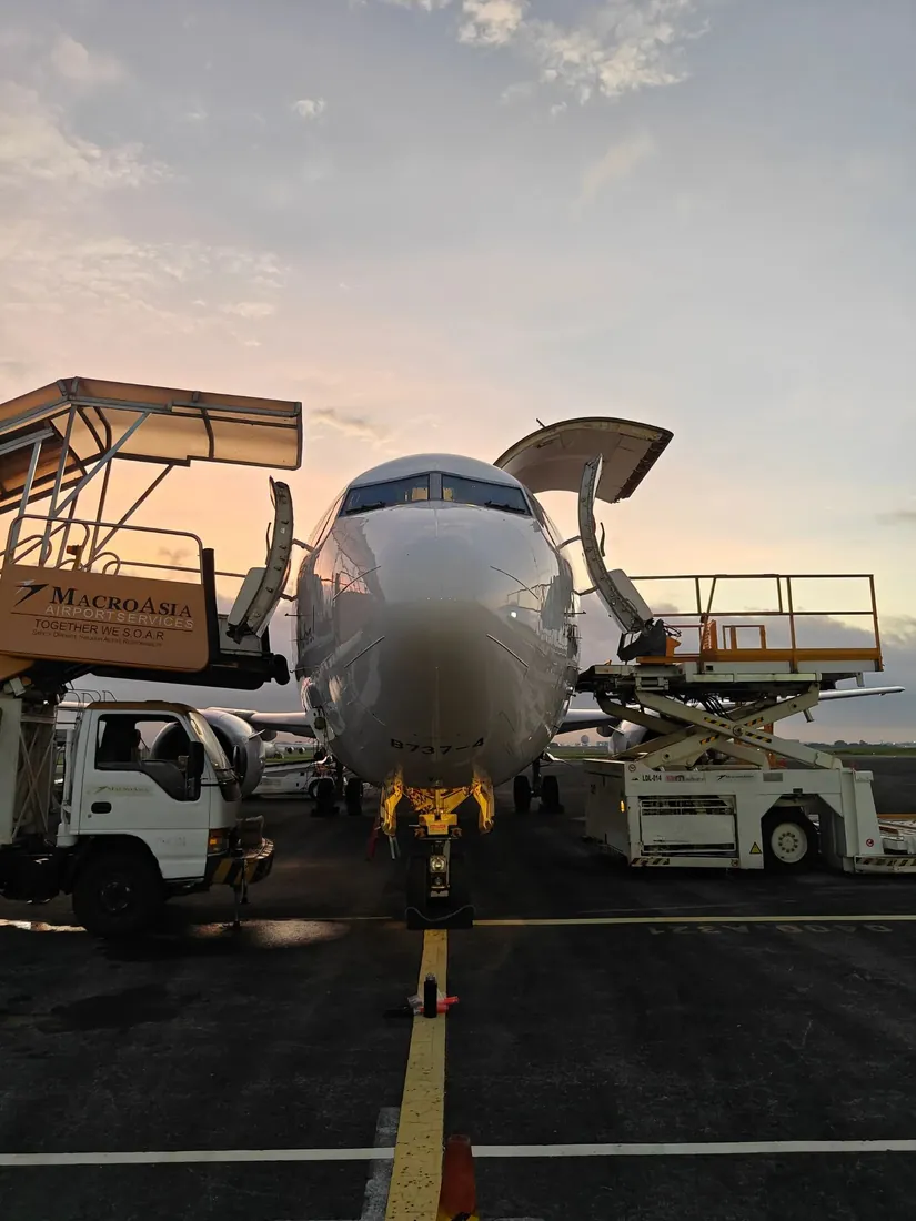 A freighter being loaded at dusk with its nose door open above a cargo loader